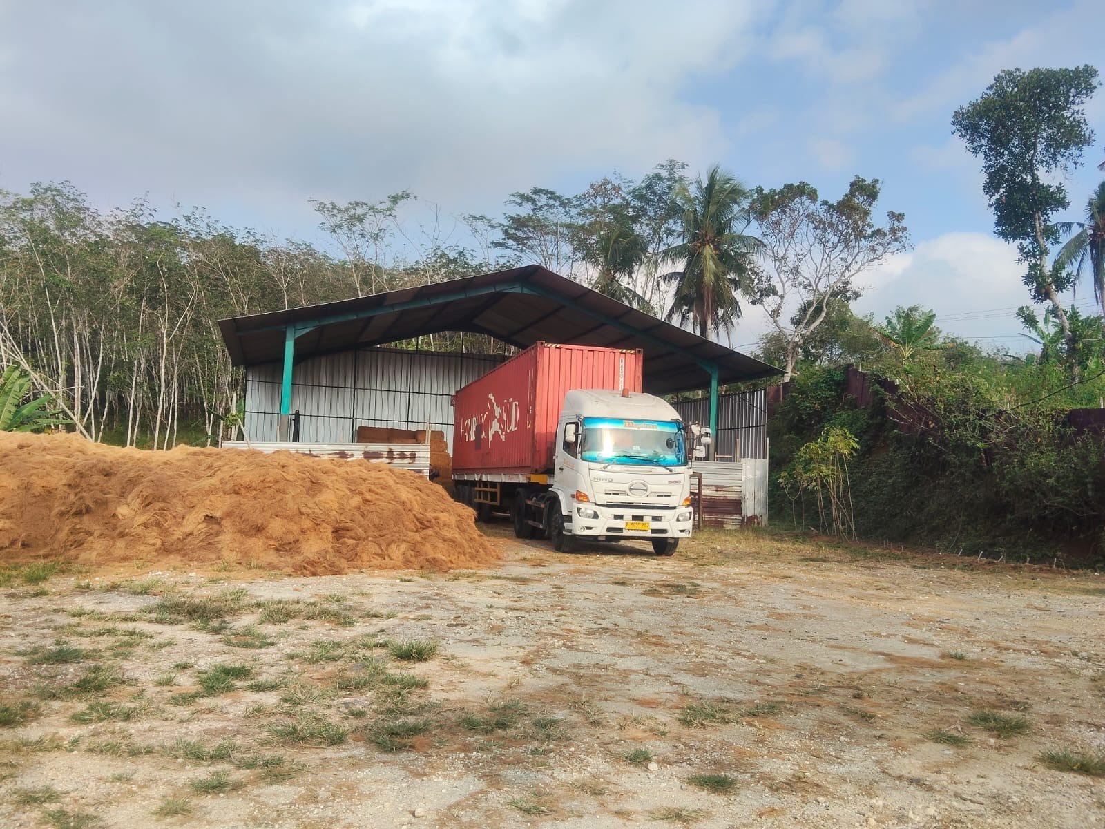 Truk kontainer dan tumpukan sabut kelapa mentah di gudang